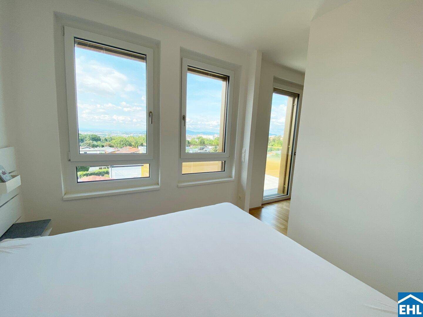 Helles Schlafzimmer mit großen Fenstern, die einen weiten Blick über die Stadt und die Natur bieten.