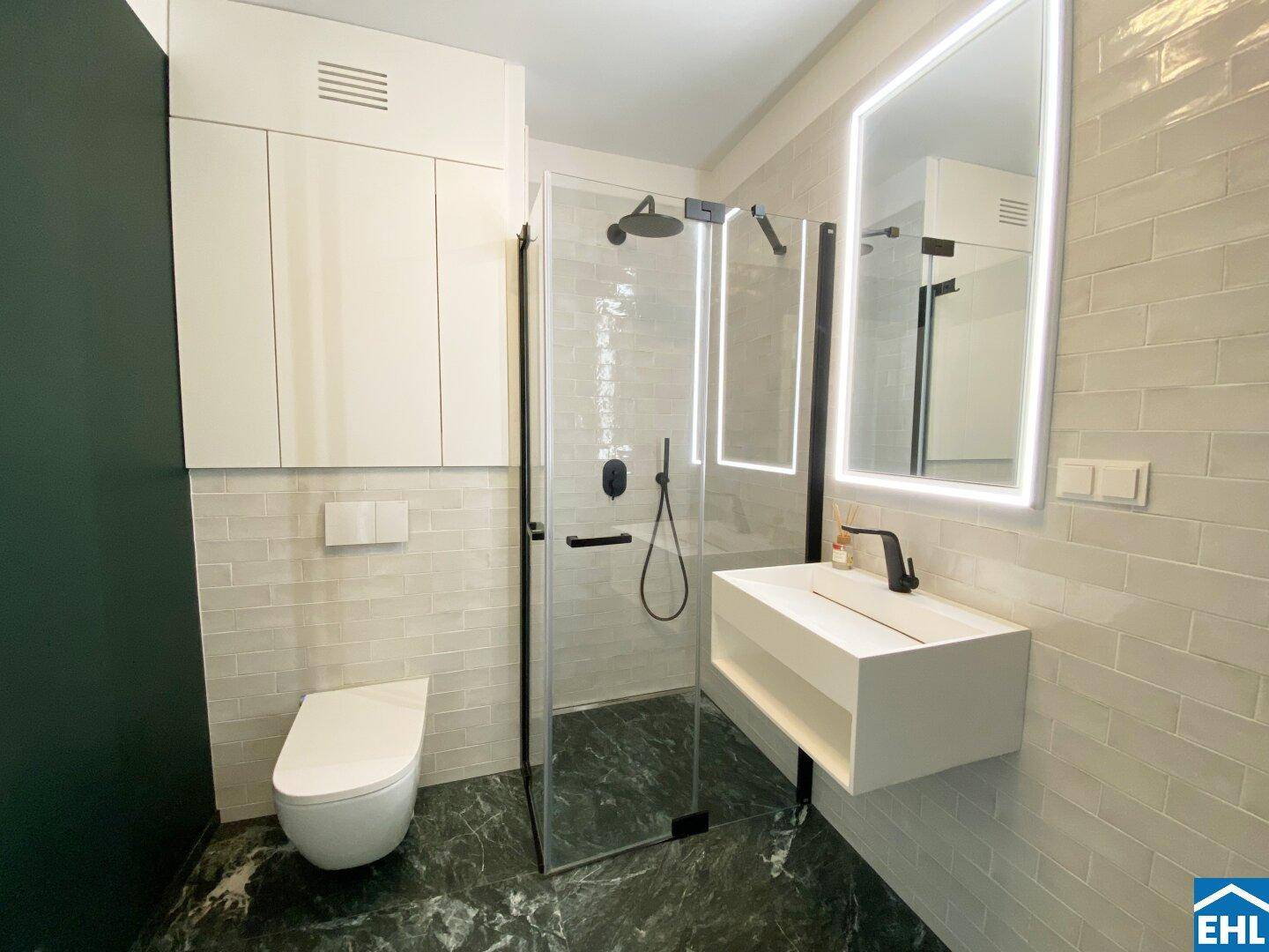 Modernes Badezimmer mit begehbarer Dusche, Wand-WC, stilvollen Fliesen und beleuchtetem Spiegel.