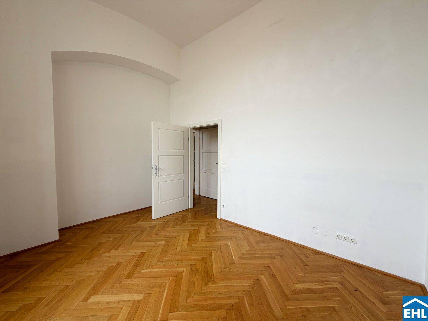 Leeres Zimmer mit Fischgrätparkett und weiß gestrichenen Wänden, bereit zur Einrichtung.