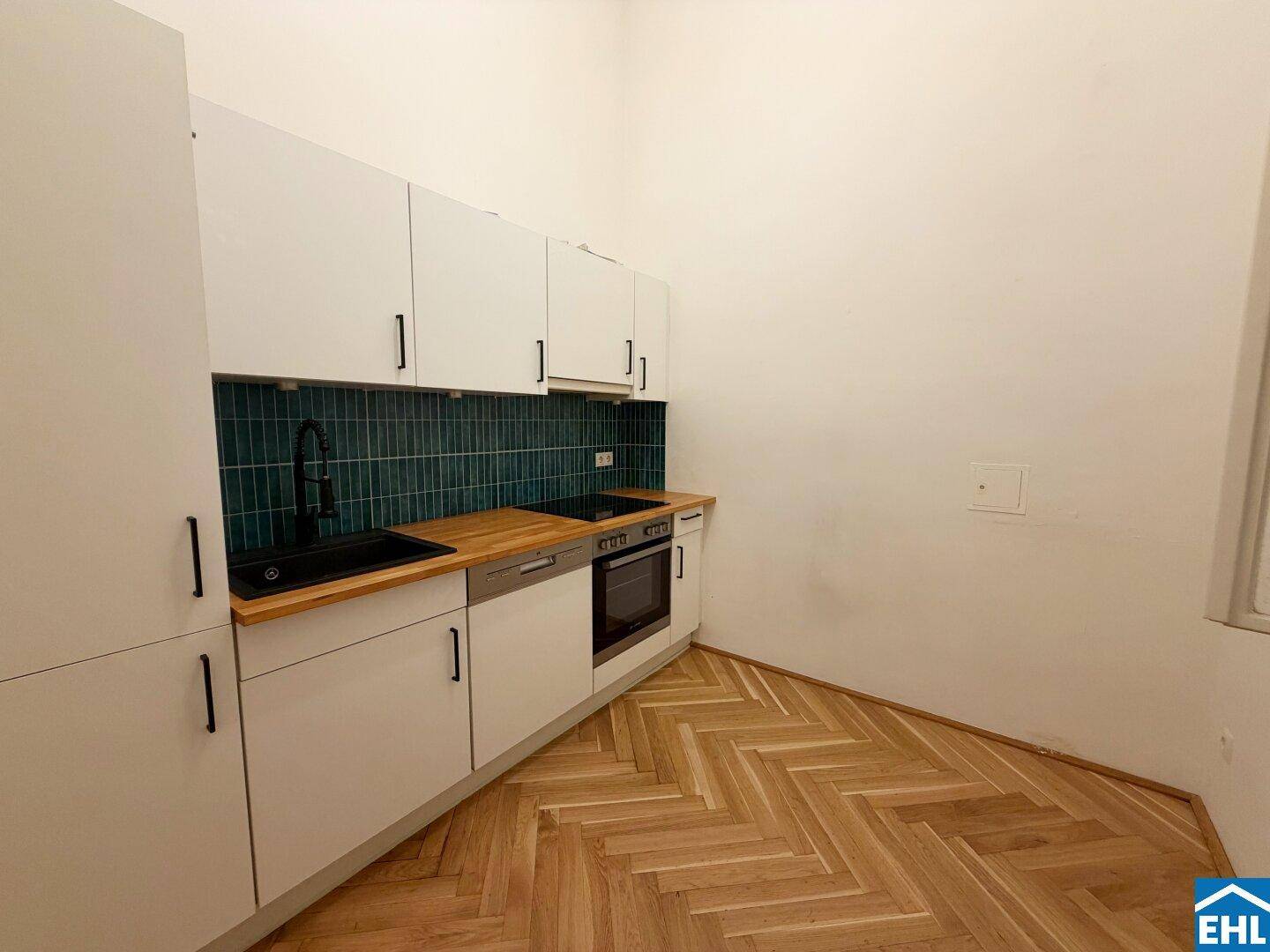 Moderne Einbauküche mit weißen Schränken, Holz-Arbeitsplatte und grünem Fliesenspiegel.