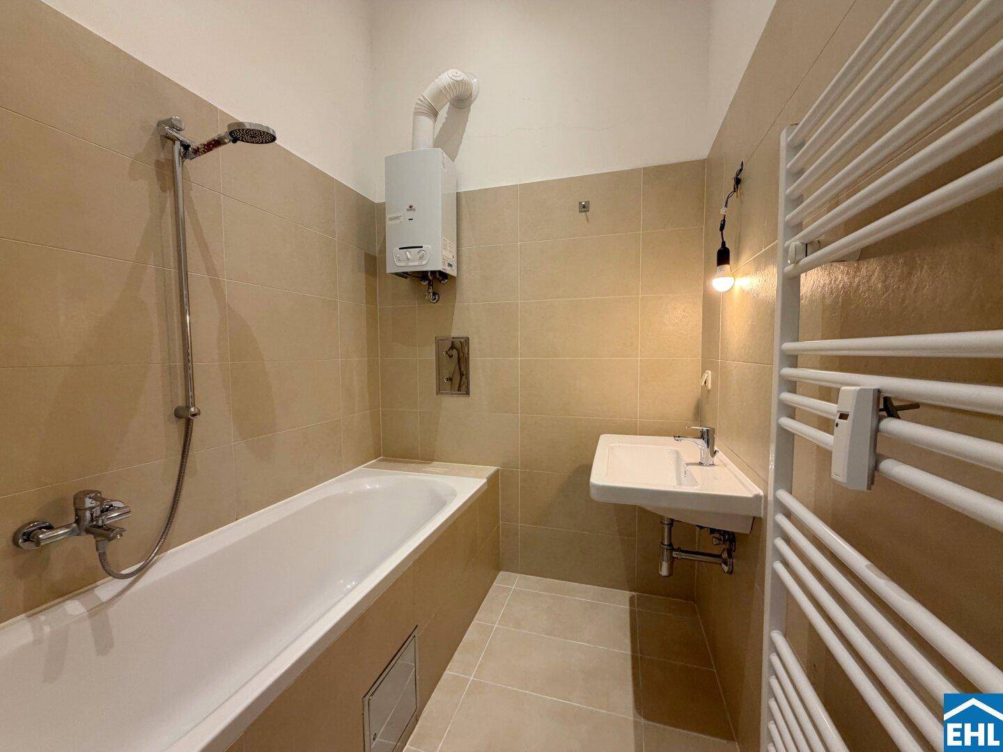 Badezimmer mit Badewanne, Waschbecken, beheiztem Handtuchhalter und beigefarbenen Fliesen.
