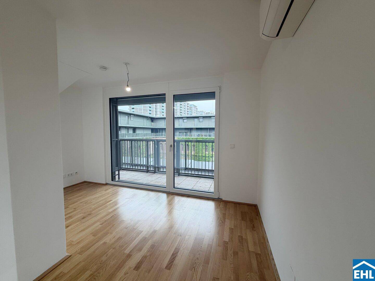 Heller Raum mit Parkettboden, weißen Wänden und Zugang zu einem Balkon.