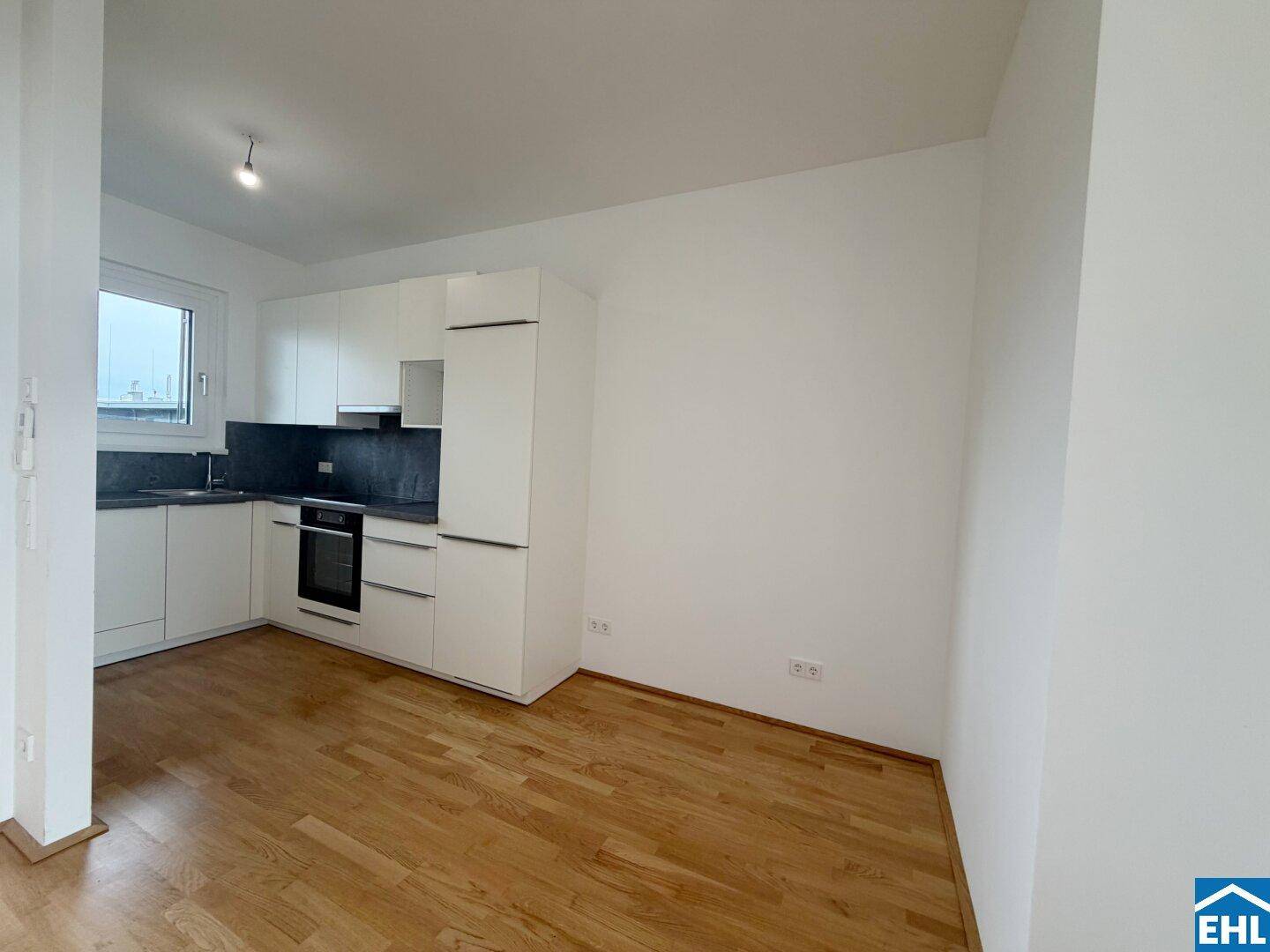 Moderner Küchenbereich mit weißen Schränken und Holzboden in einem hellen Raum.