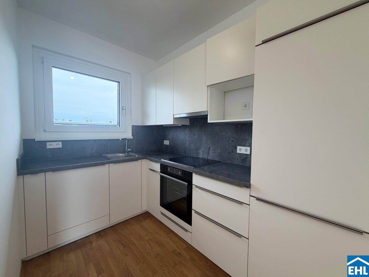 Moderne Einbauküche mit weißen Fronten, dunkler Arbeitsplatte und integrierten Geräten.