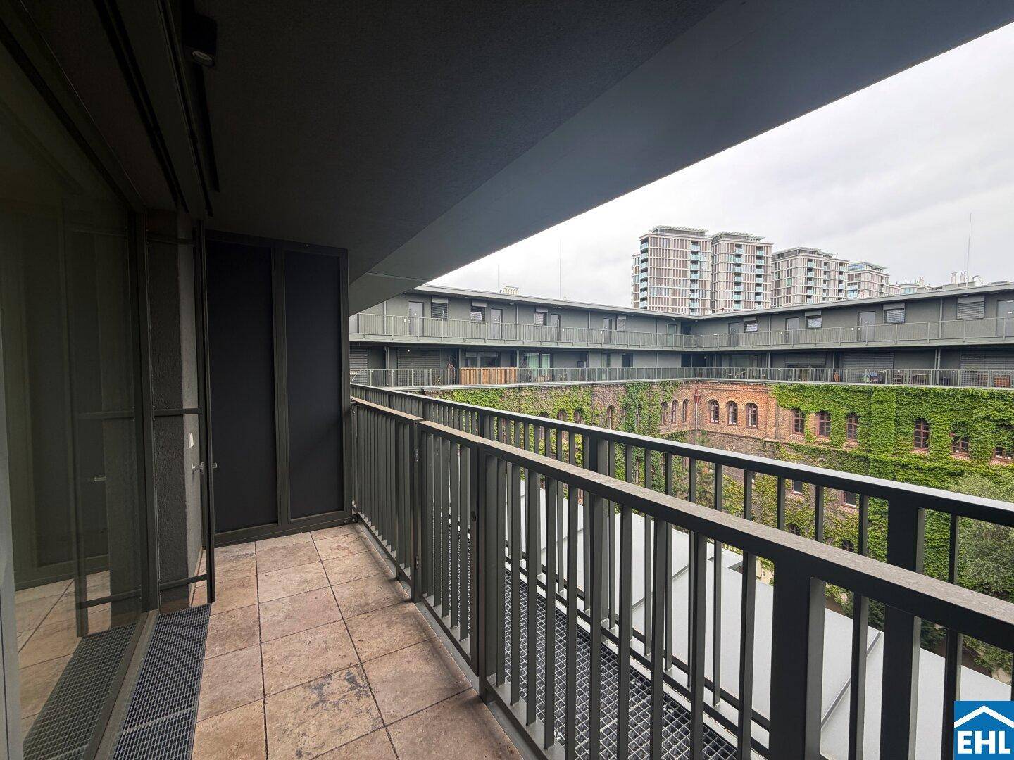 Überdachter Balkon mit Fliesenboden und Blick auf einen begrünten Innenhof.