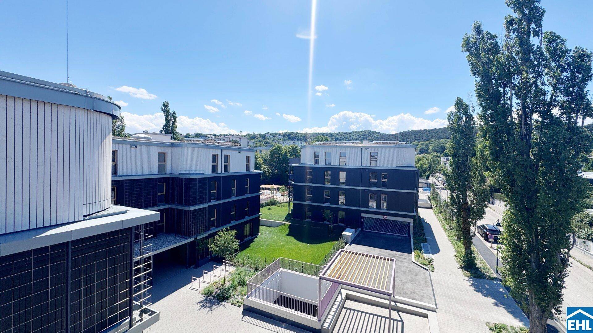 Panoramablick auf moderne Wohngebäude mit Grünflächen und einer Straße unter blauem Himmel.