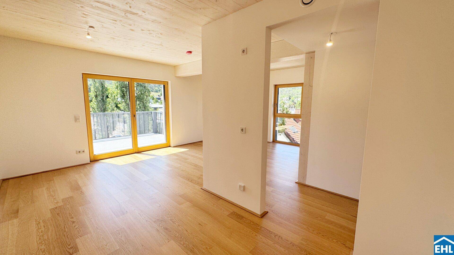 Geräumiger, heller Innenraum mit Holzboden und Blick auf den Außenbereich durch große Fenster.