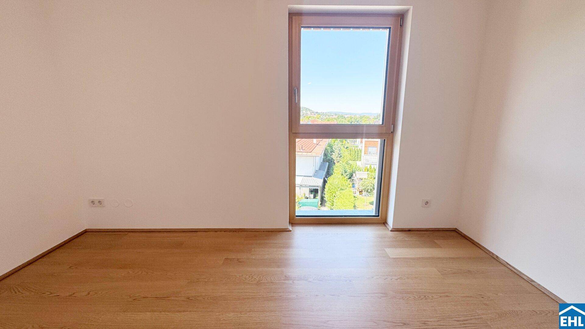 Helles Zimmer mit Holzboden und einem großen Fenster, das einen weiten Blick ins Grüne bietet.