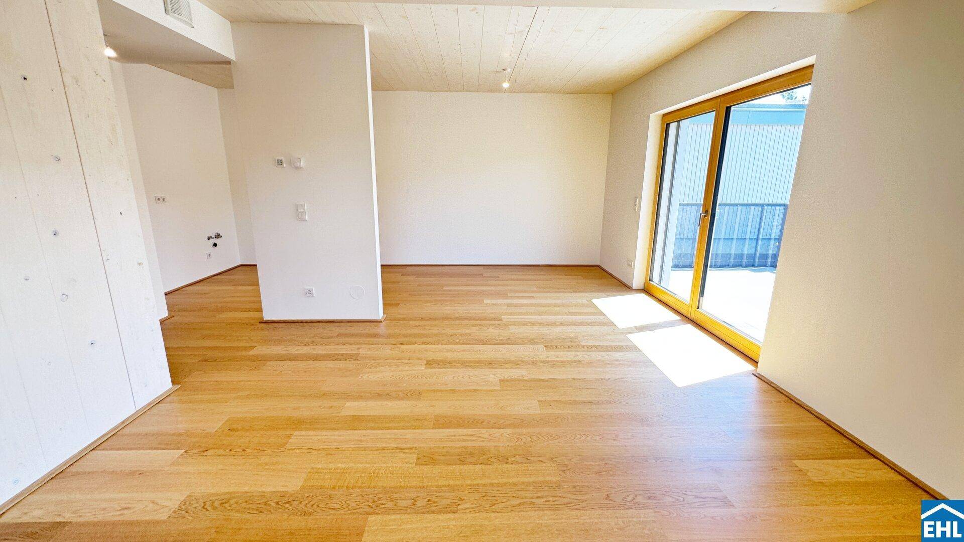 Lichtdurchfluteter Wohnbereich mit Holzboden und Schiebetür, die zu einem Außenbereich führt.