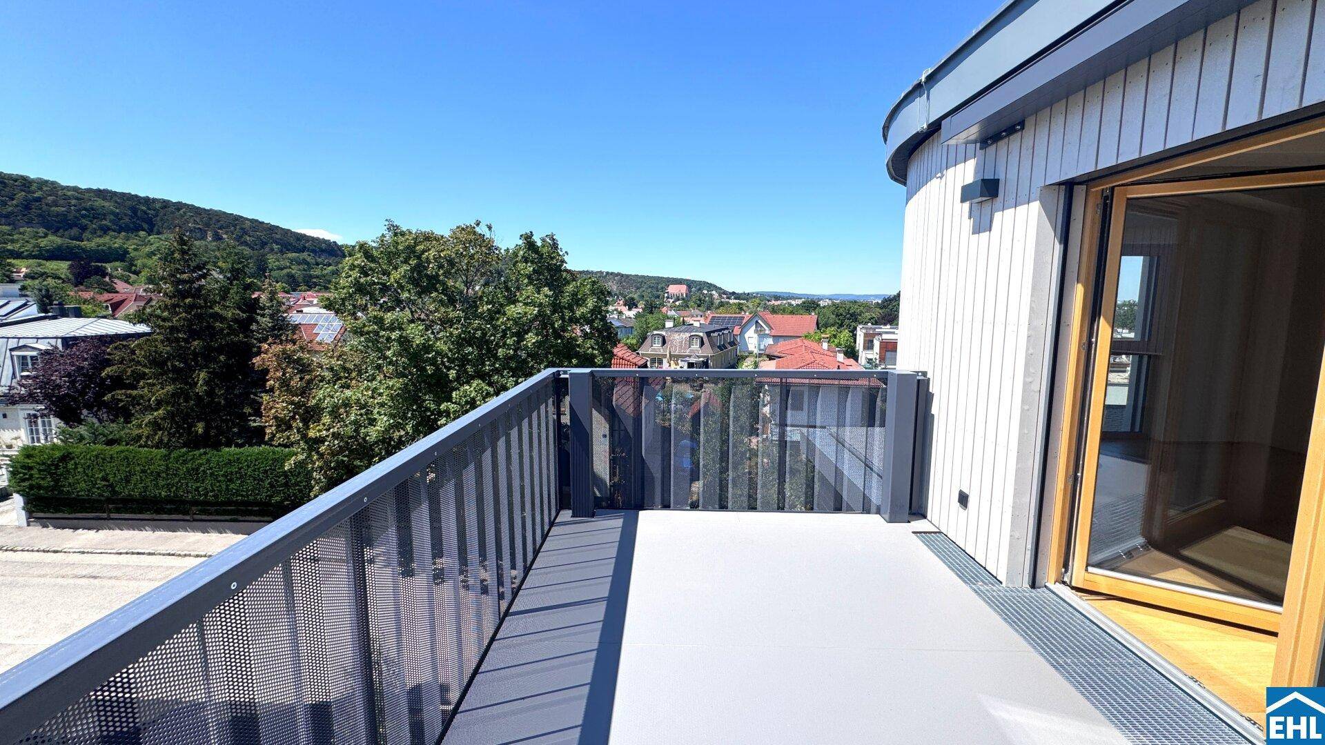 Geräumiger Balkon mit moderner Brüstung und weitem Blick über die Stadt und grüne Hügel.