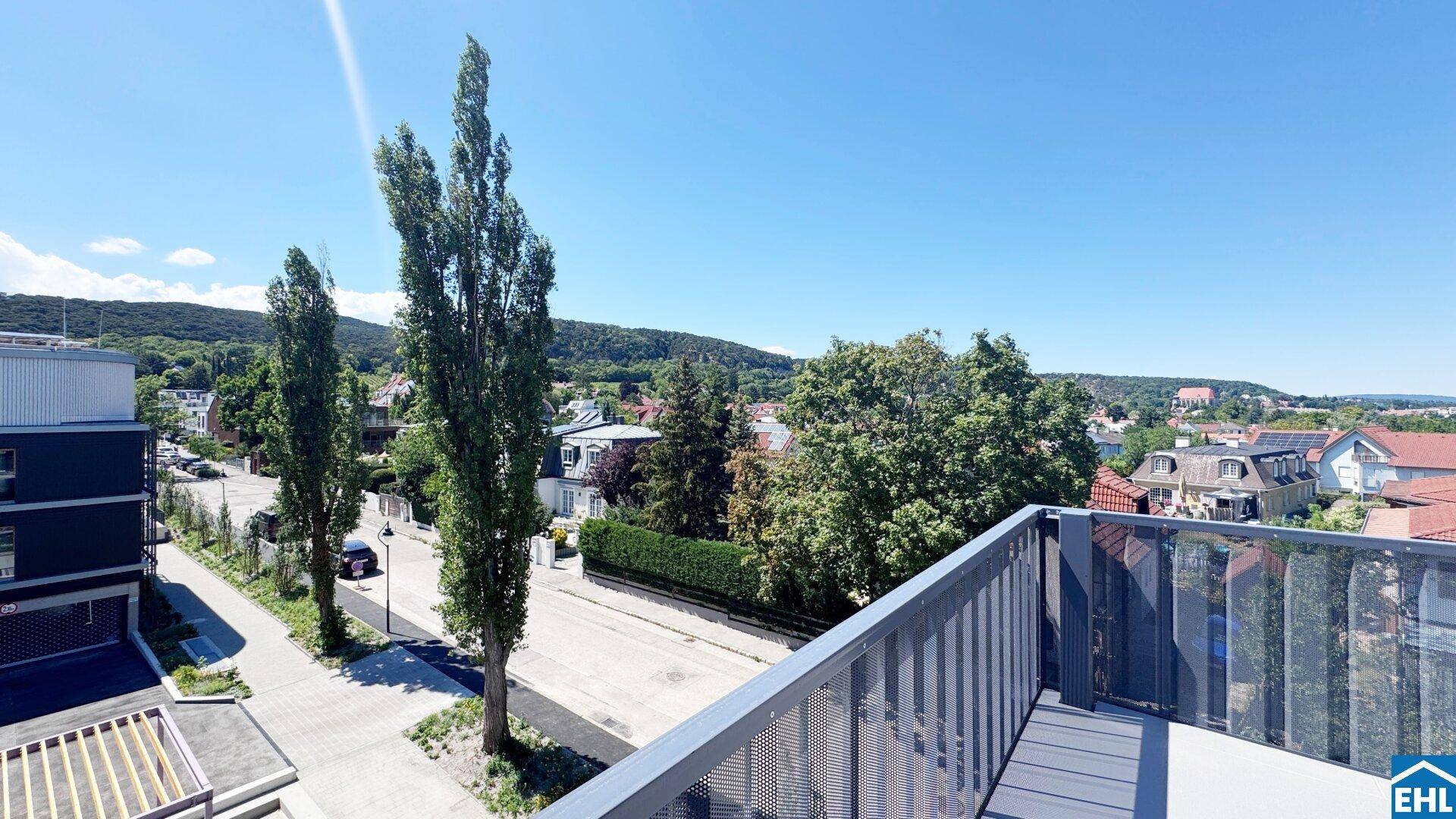 Sonniger Balkon mit Blick auf die umliegende Wohngegend und die bewaldeten Hügel in der Ferne.