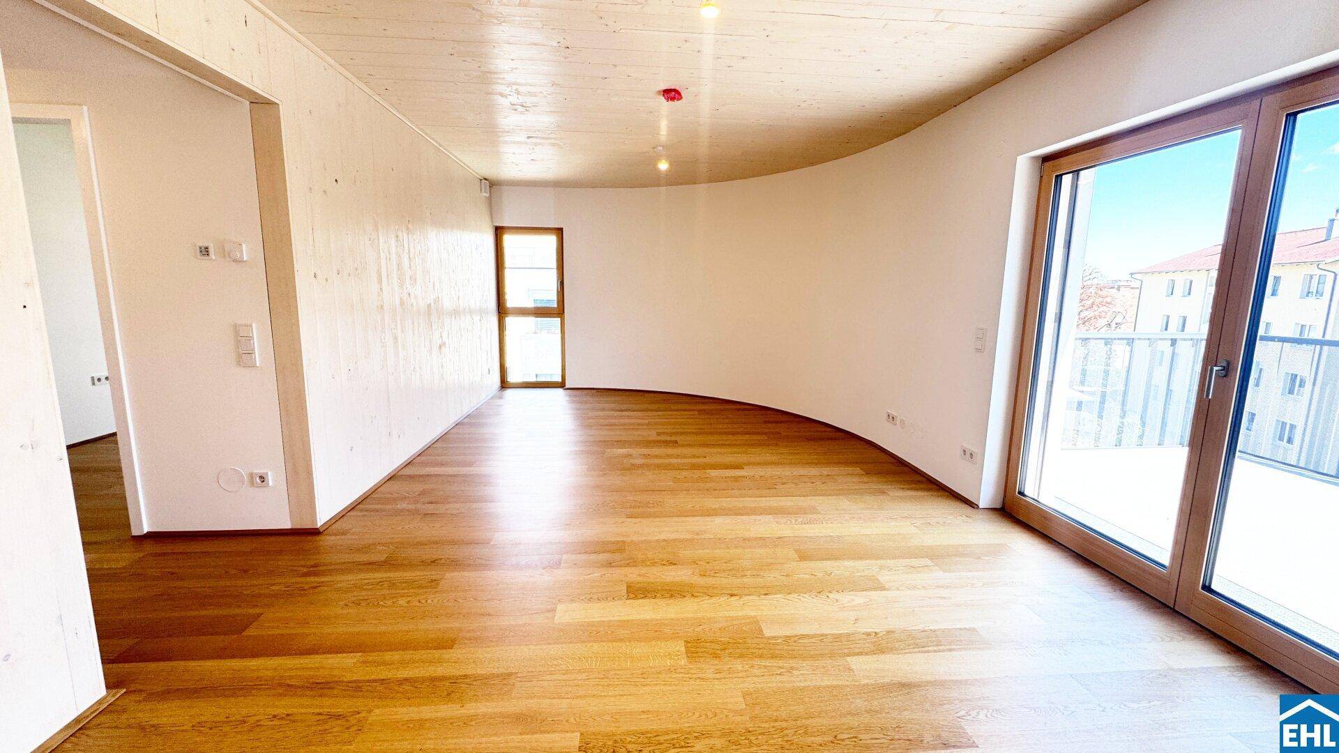 Geräumiges Wohnzimmer mit geschwungener Wand, Holzboden und großen Fenstern, die viel Licht hereinlassen.