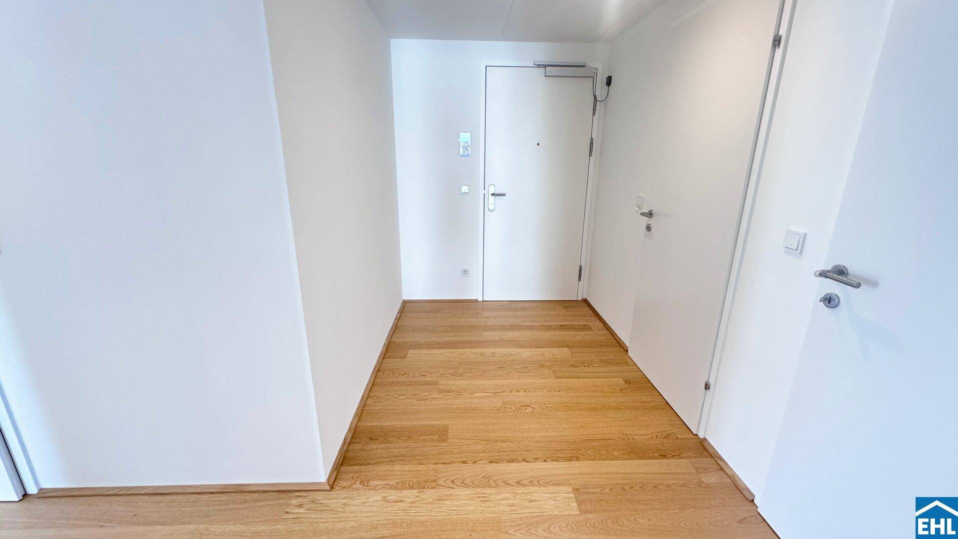 Heller Eingangsbereich mit Holzboden und weißen Wänden, der zu den verschiedenen Zimmern führt.