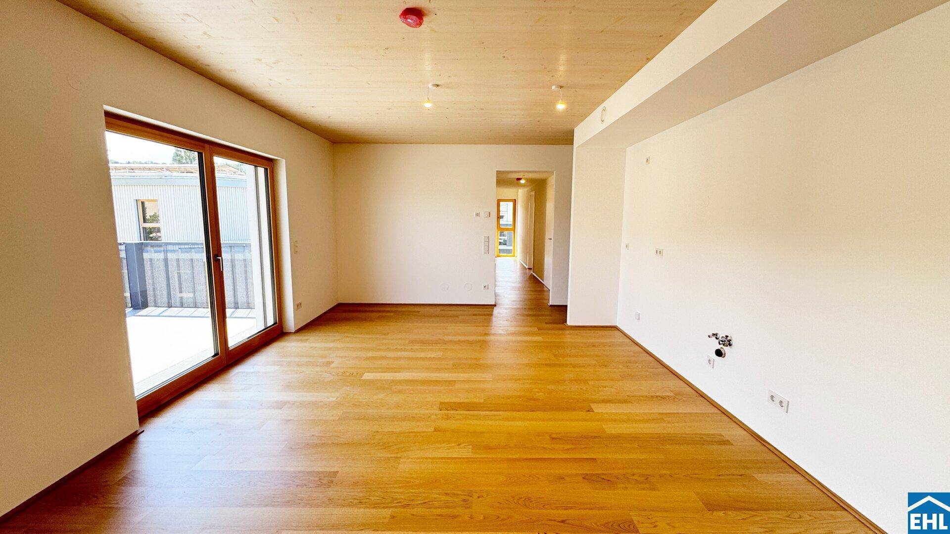 Geräumiges, leeres Zimmer mit Holzboden und Holzdecke, das zu einem Flur führt und Balkonzugang bietet.