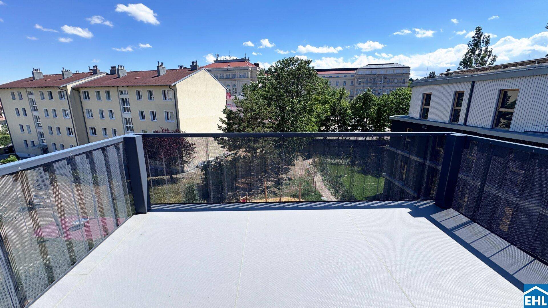 Geräumiger Balkon mit modernem Geländer und Blick auf umliegende Gebäude und grüne Bäume.