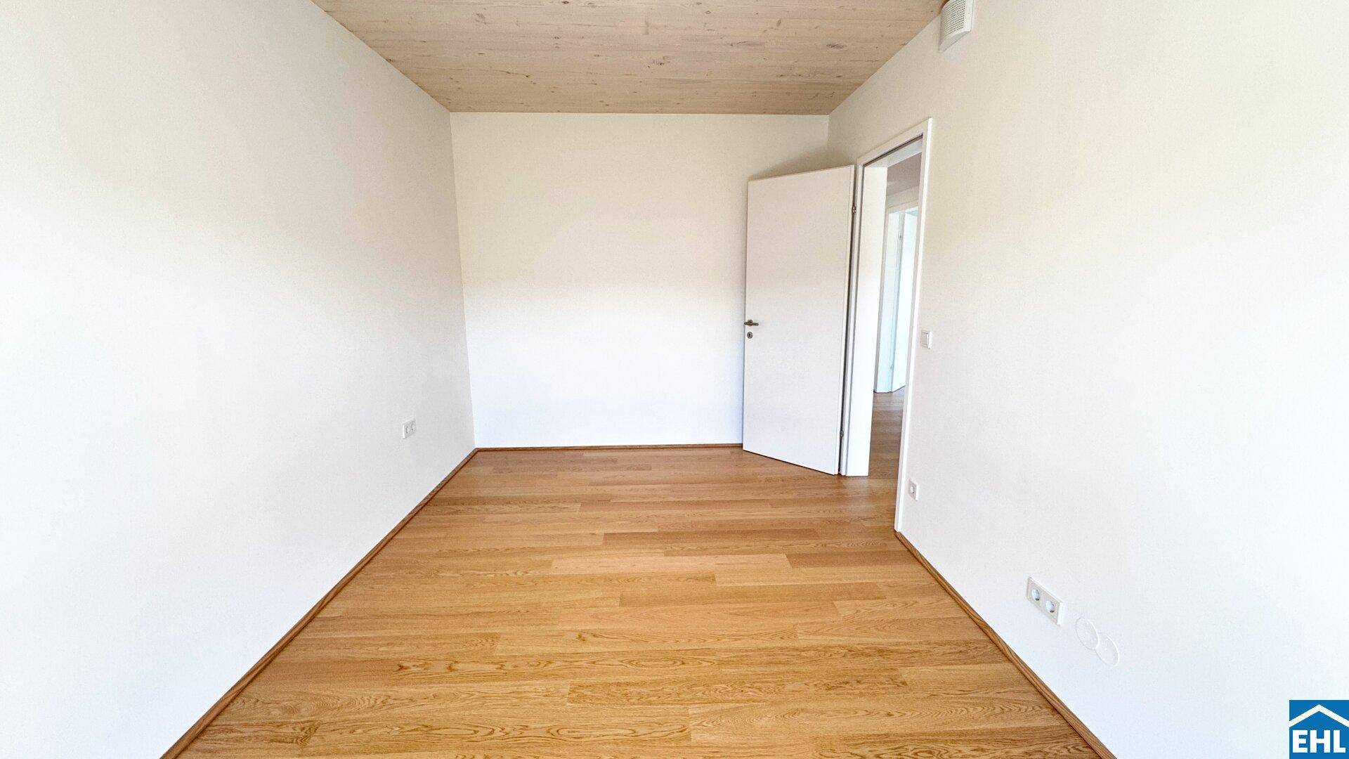 Unmöblierter Raum mit Holzboden, Holzdecke und einer offenen Tür, bereit zum Einzug.