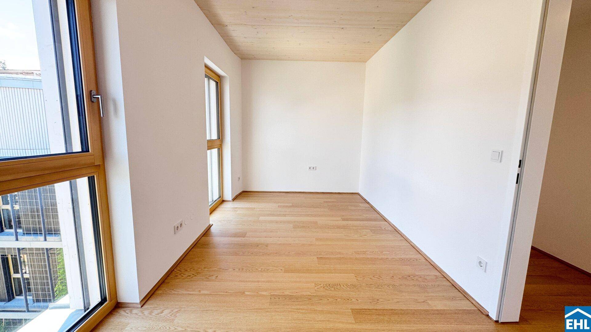 Helles Schlafzimmer mit Holzboden, Holzdecke und großen Fenstern mit Blick nach draußen.