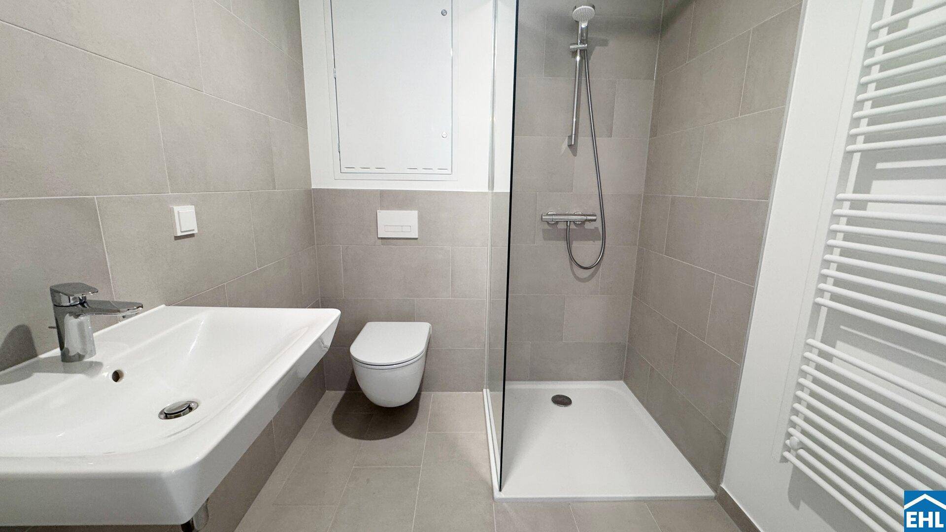 Modernes Badezimmer mit ebenerdiger Dusche, wandhängendem WC und Waschbecken.