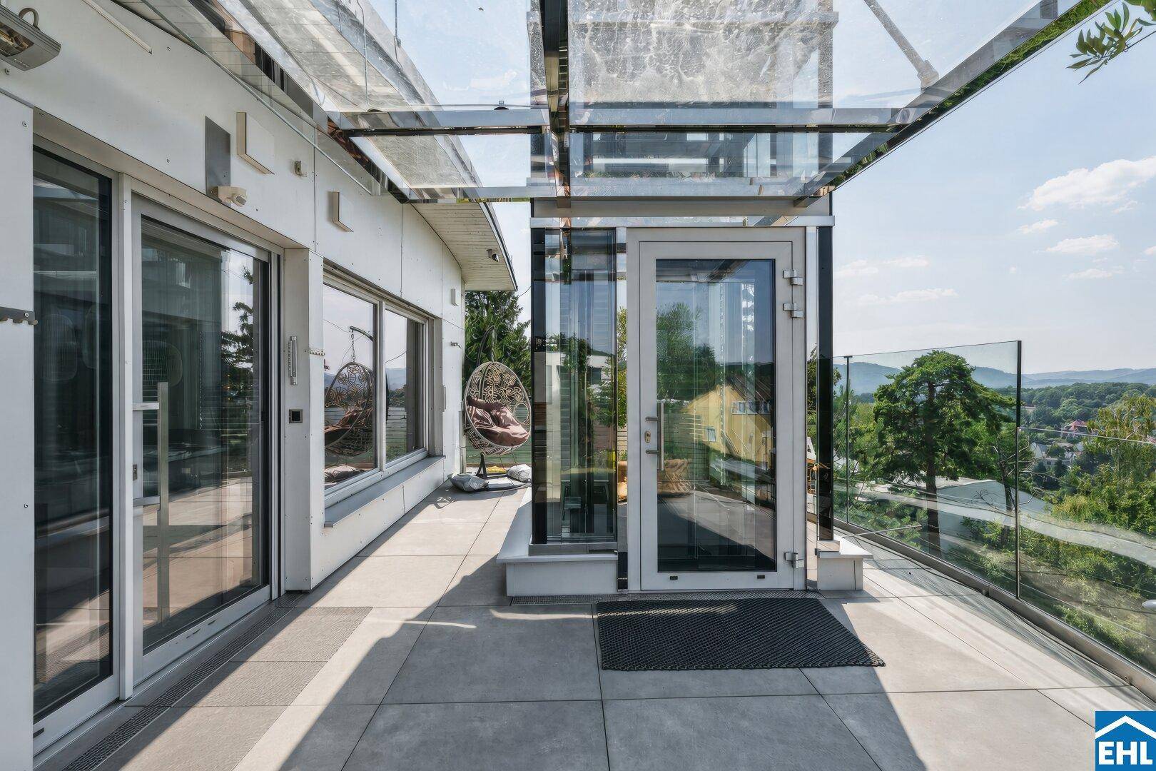 Geräumige Terrasse mit Glasgeländer und weitem Blick über die hügelige Landschaft.