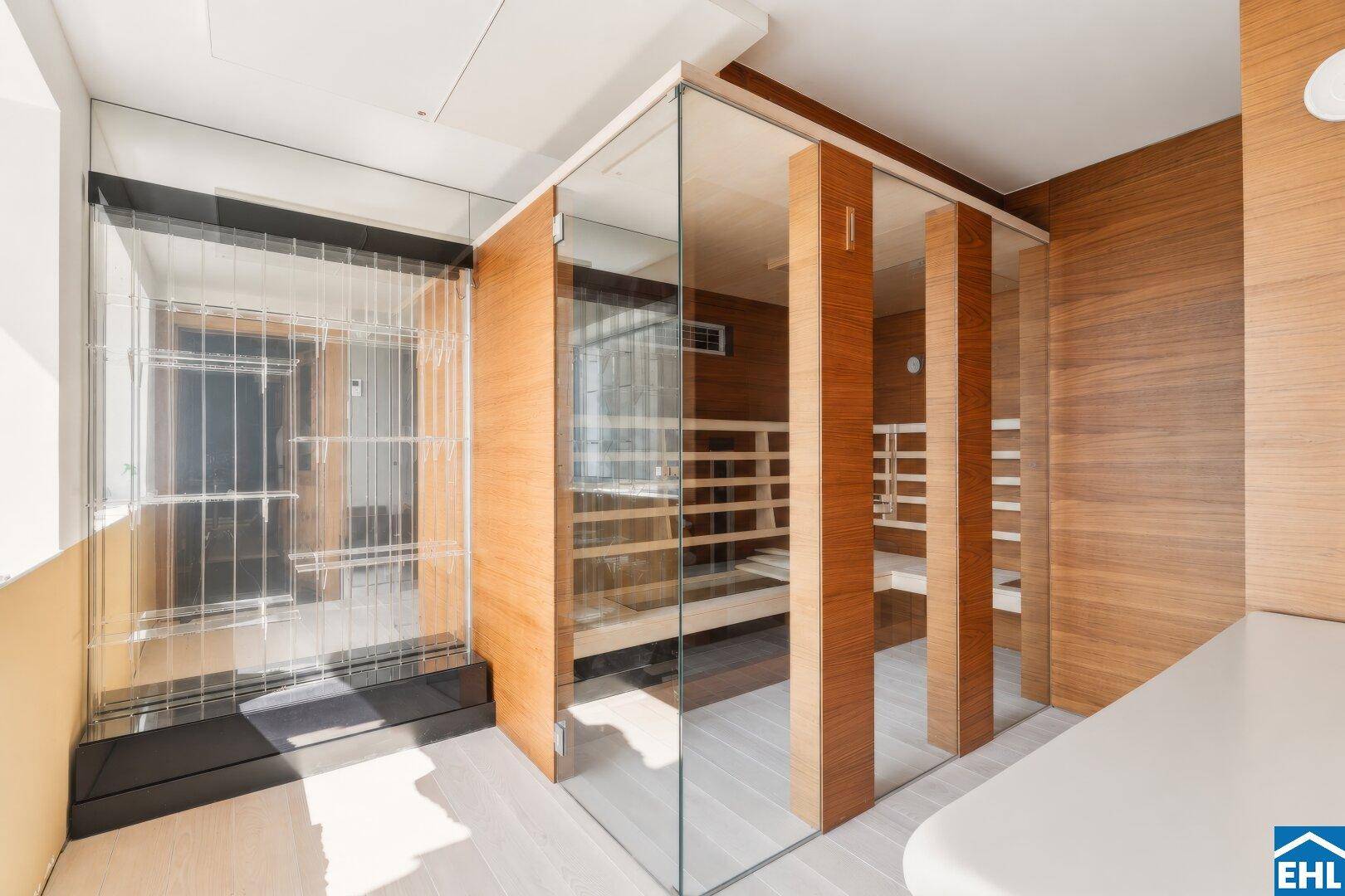 Moderner Wellnessbereich mit verglaster Sauna und Dampfdusche, umgeben von Holzverkleidung.
