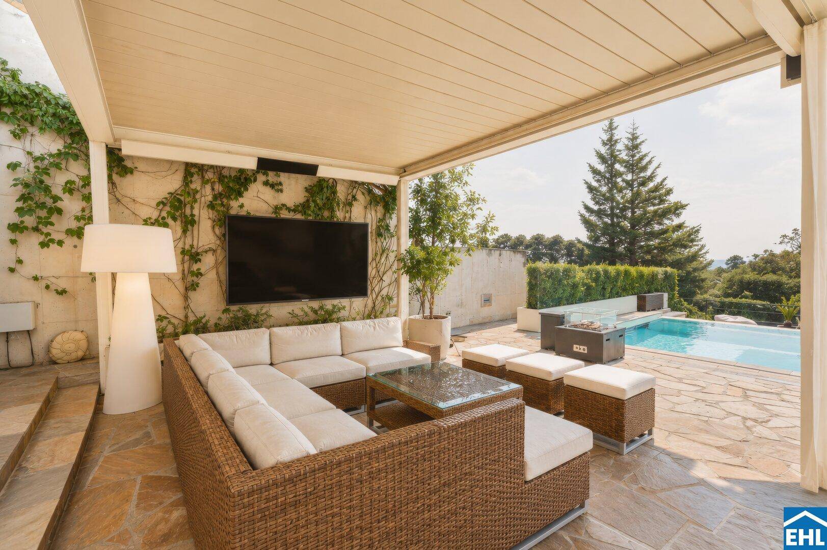 Überdachter Loungebereich im Freien mit bequemen Sofas, Fernseher und direktem Zugang zum Pool.