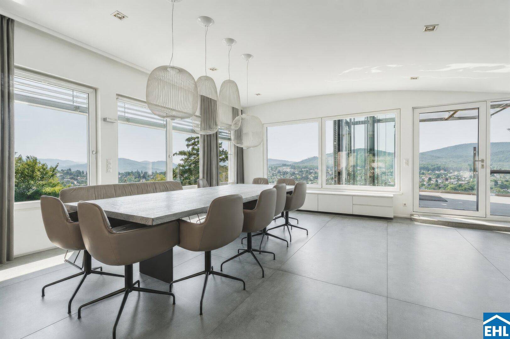 Heller Essbereich mit großem Tisch, modernen Pendelleuchten und Panoramablick auf die Landschaft.