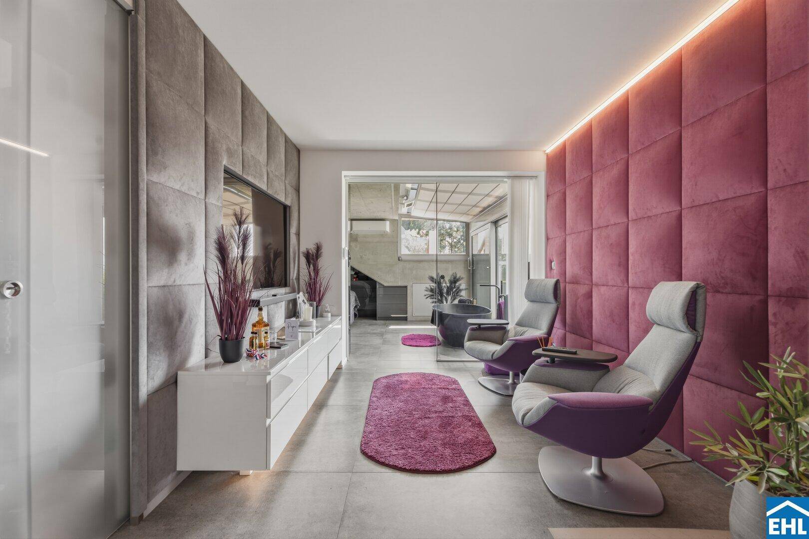 Stilvoller Loungebereich mit modernen Sesseln, Fernseher und einer auffälligen, gepolsterten Wand.