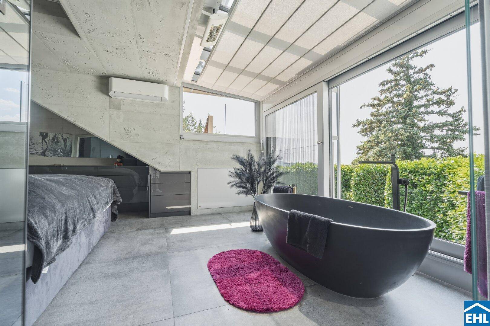 Schlafzimmer mit freistehender Badewanne und großen Fenstern, die einen grünen Ausblick bieten.