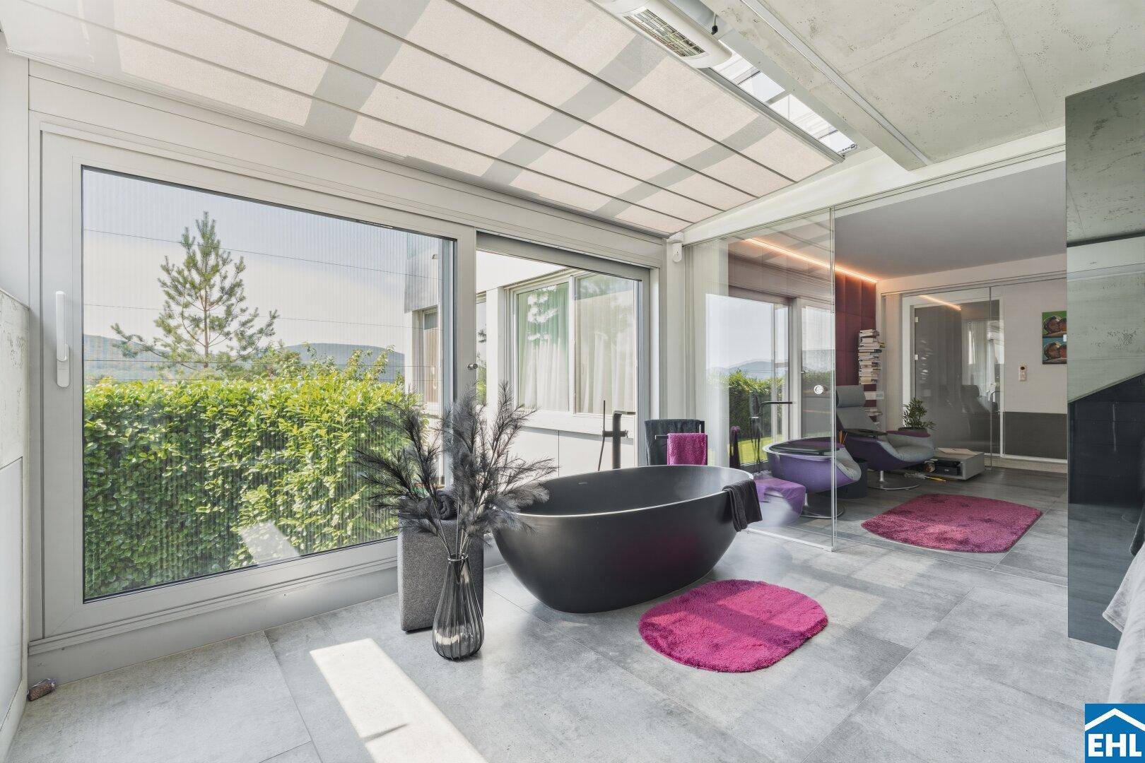 Helles Schlafzimmer mit offener Badewanne und weitem Blick ins Grüne durch große Fensterfronten.
