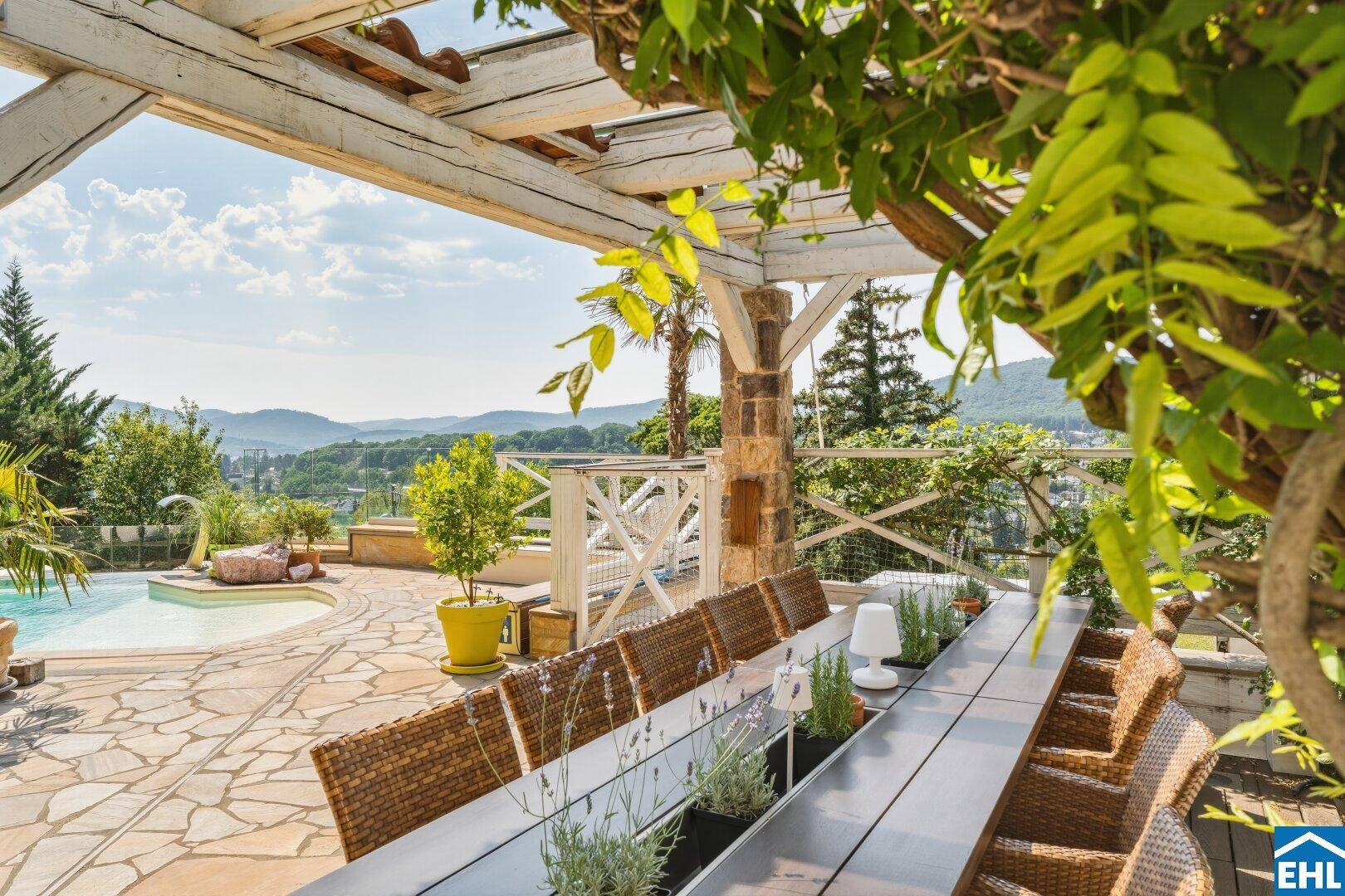 Gemütlicher Essbereich im Freien unter einer Pergola mit Blick auf den Pool und die Landschaft.