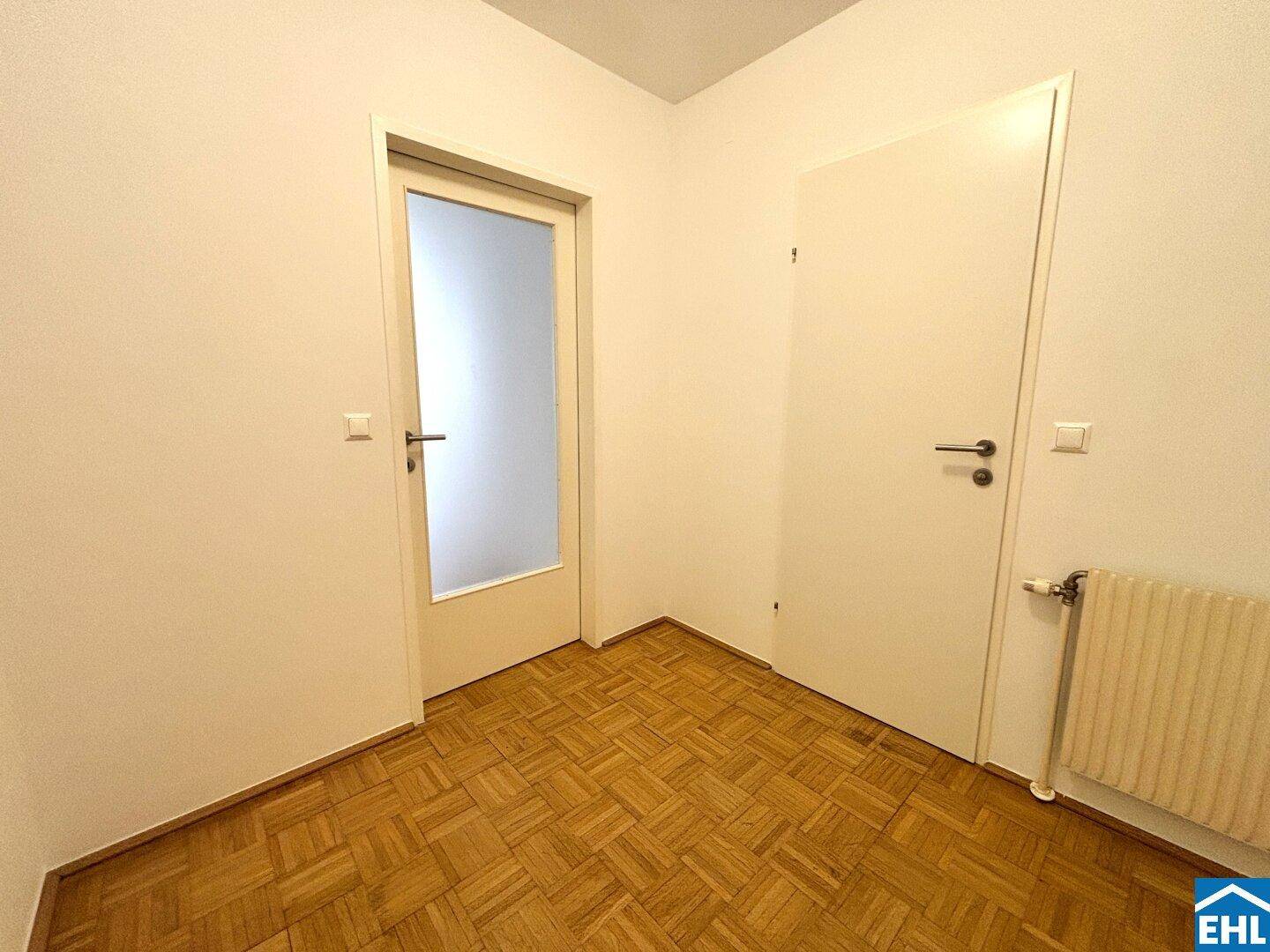 Heller Flur mit Parkettboden und zwei Türen, eine davon mit Glaseinsatz.