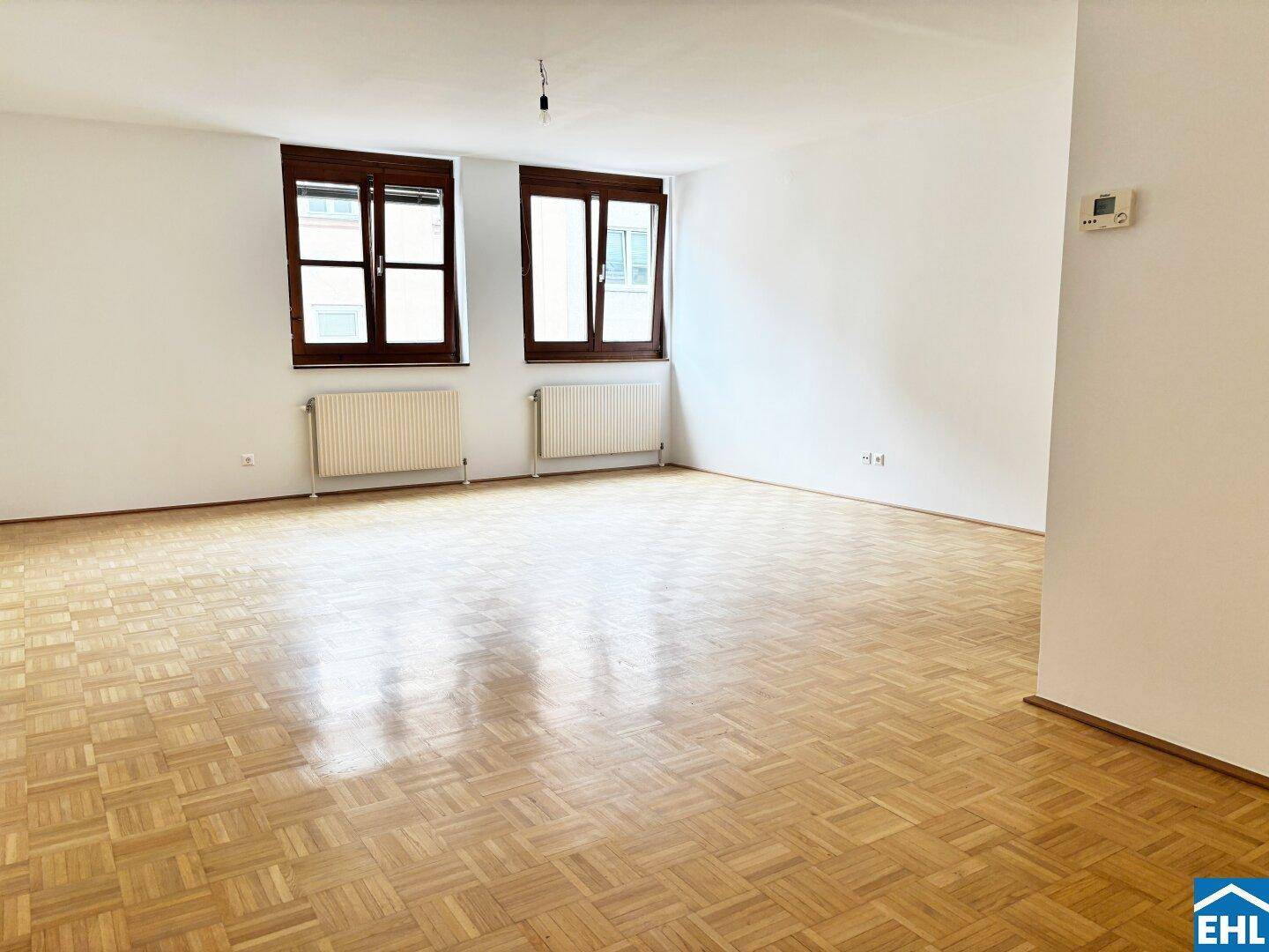 Heller Wohnbereich mit Parkettboden und zwei Fenstern, bereit zur individuellen Gestaltung.