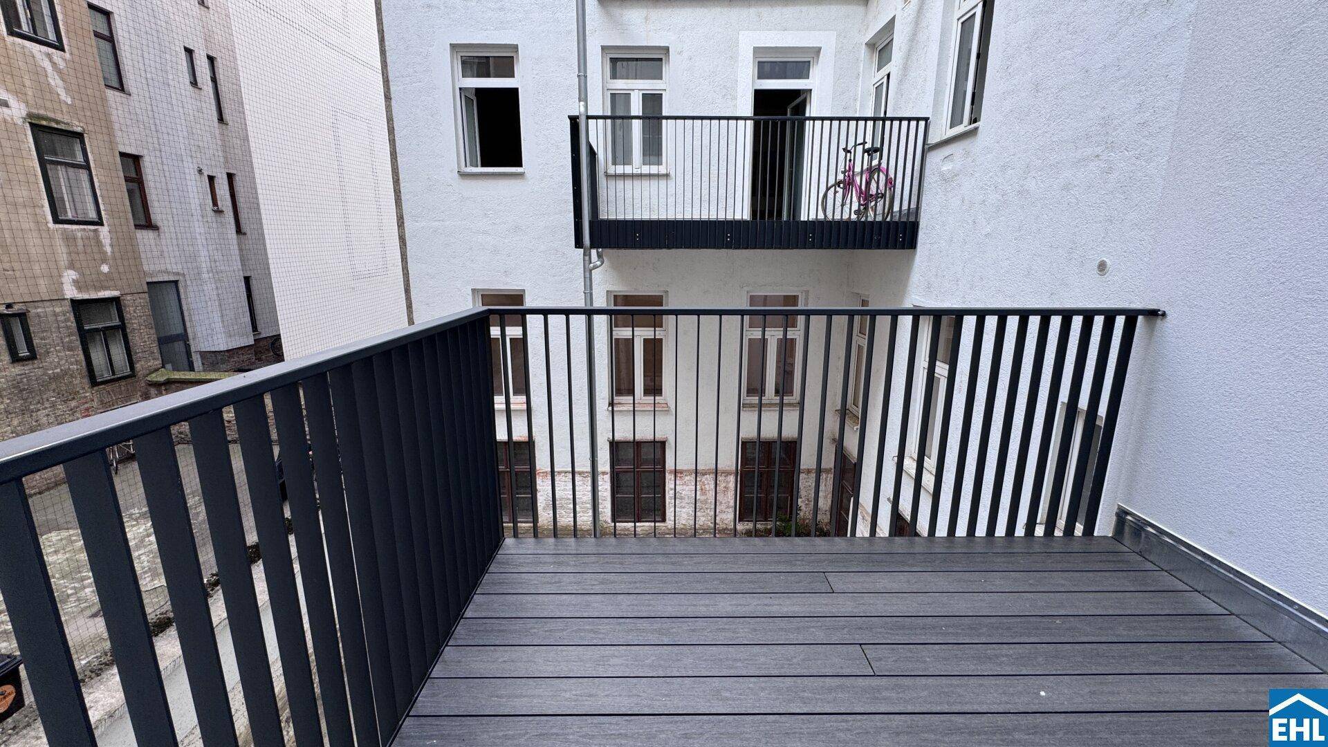 Moderner Balkon mit dunklem Bodenbelag und schwarzem Geländer, mit Blick auf den Innenhof.