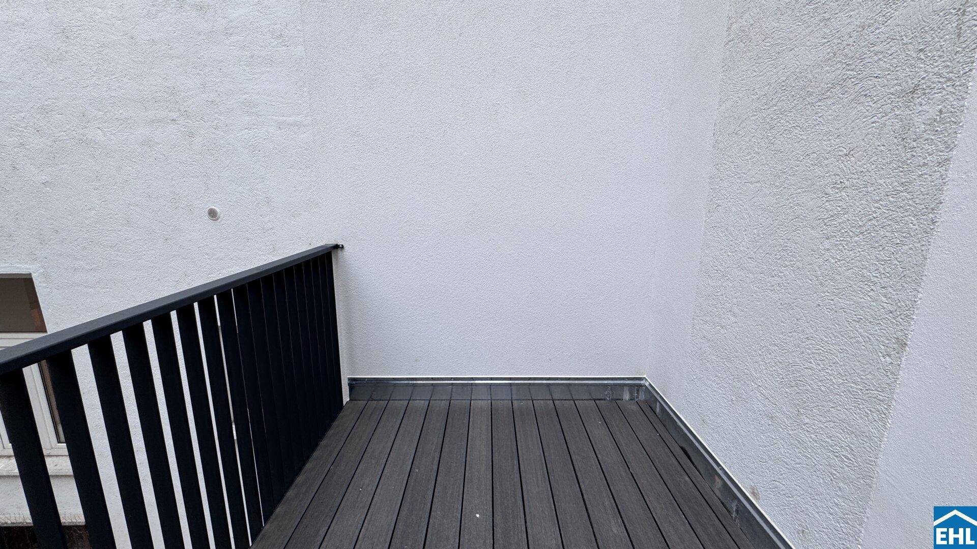 Neuer Balkon mit dunklem WPC-Boden und schlichtem schwarzen Geländer an einer weißen Fassade.