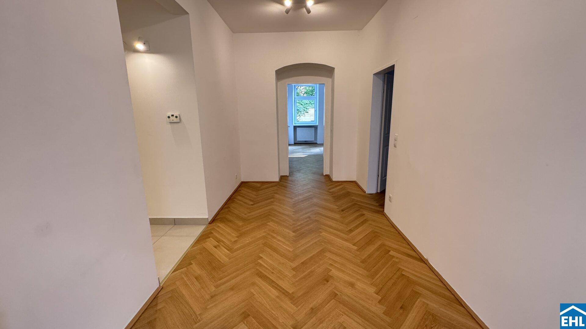 Langer Flur mit elegantem Fischgrätparkett und einem Bogen, der zu einem weiteren Zimmer führt.