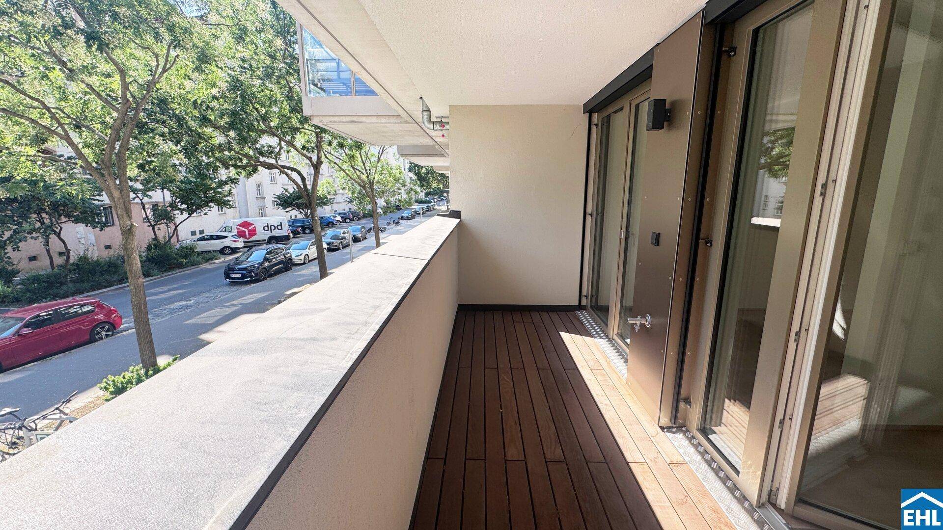 Geräumiger Balkon mit Holzdielen und weitem Blick entlang der Baumallee und der Straße.