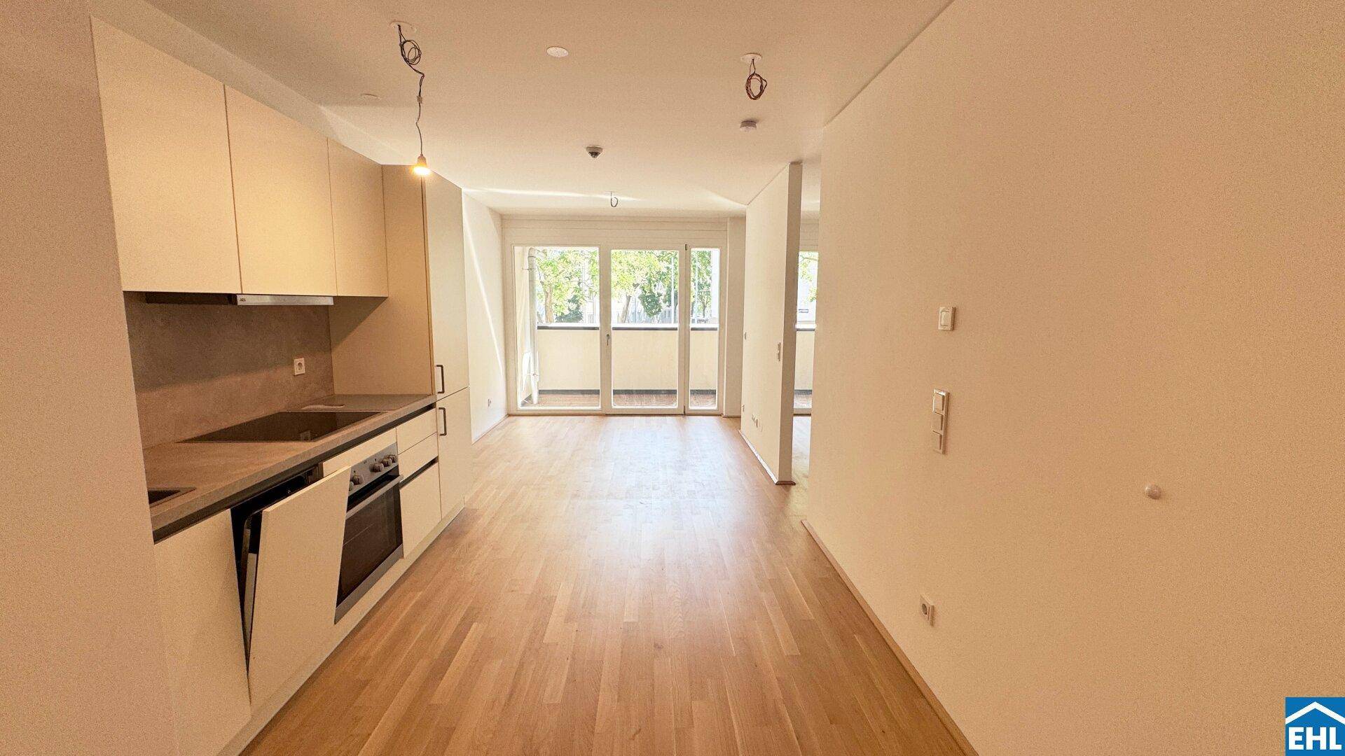 Offener Wohnbereich mit integrierter Küchenzeile, Holzboden und Zugang zu einem Balkon.