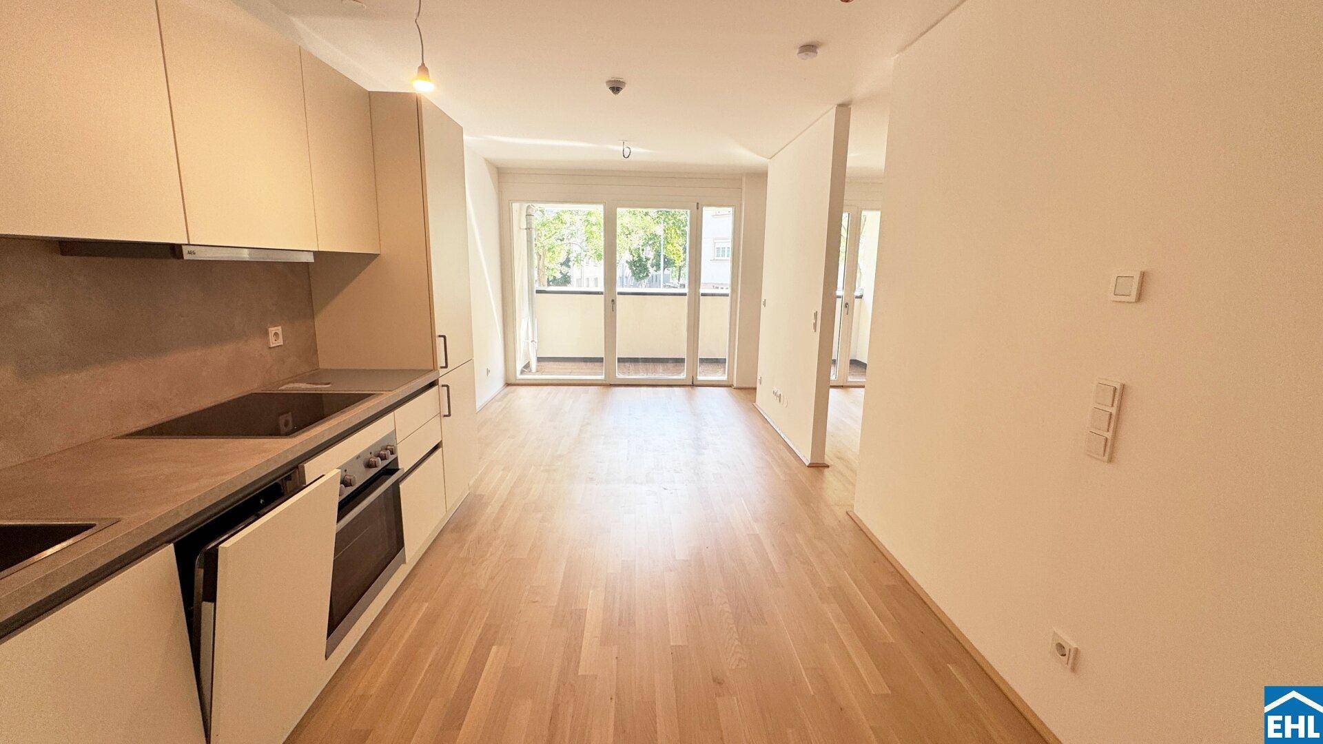 Heller Wohnbereich mit moderner Küchenzeile, Parkettboden und großen Fenstern zum Balkon.