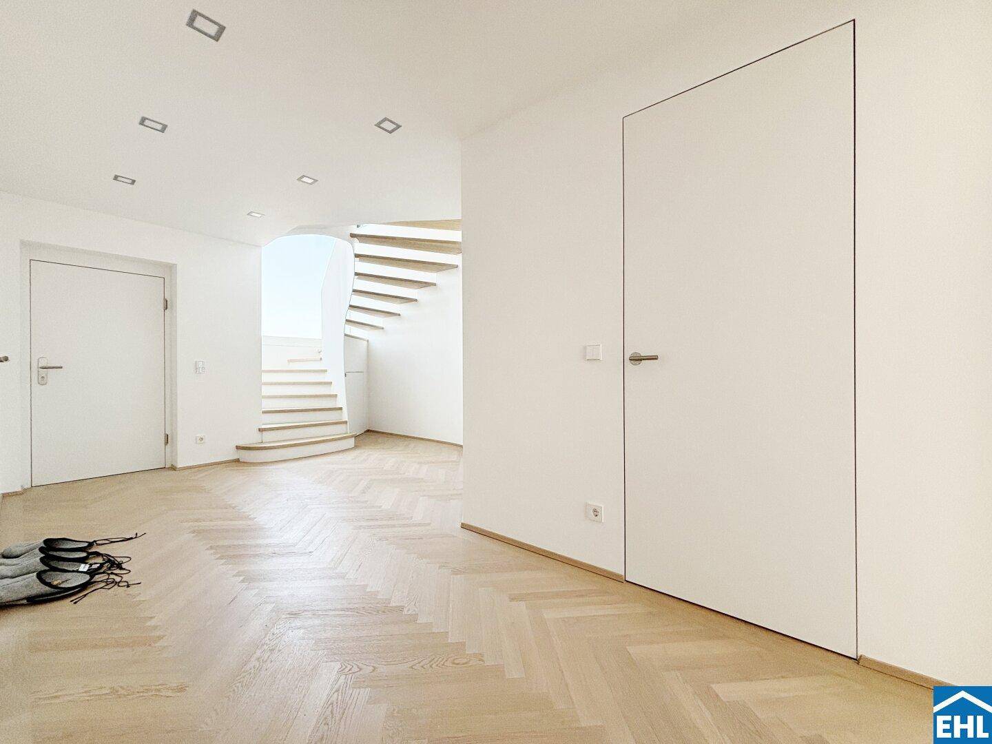 Heller Eingangsbereich mit Fischgrätparkett und eleganter, offener Treppe.