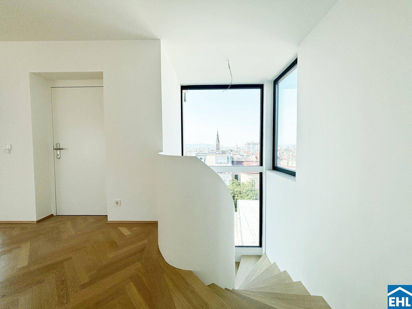 Elegantes Treppenhaus mit großen Fenstern, die einen weiten Blick über die Stadt bieten.