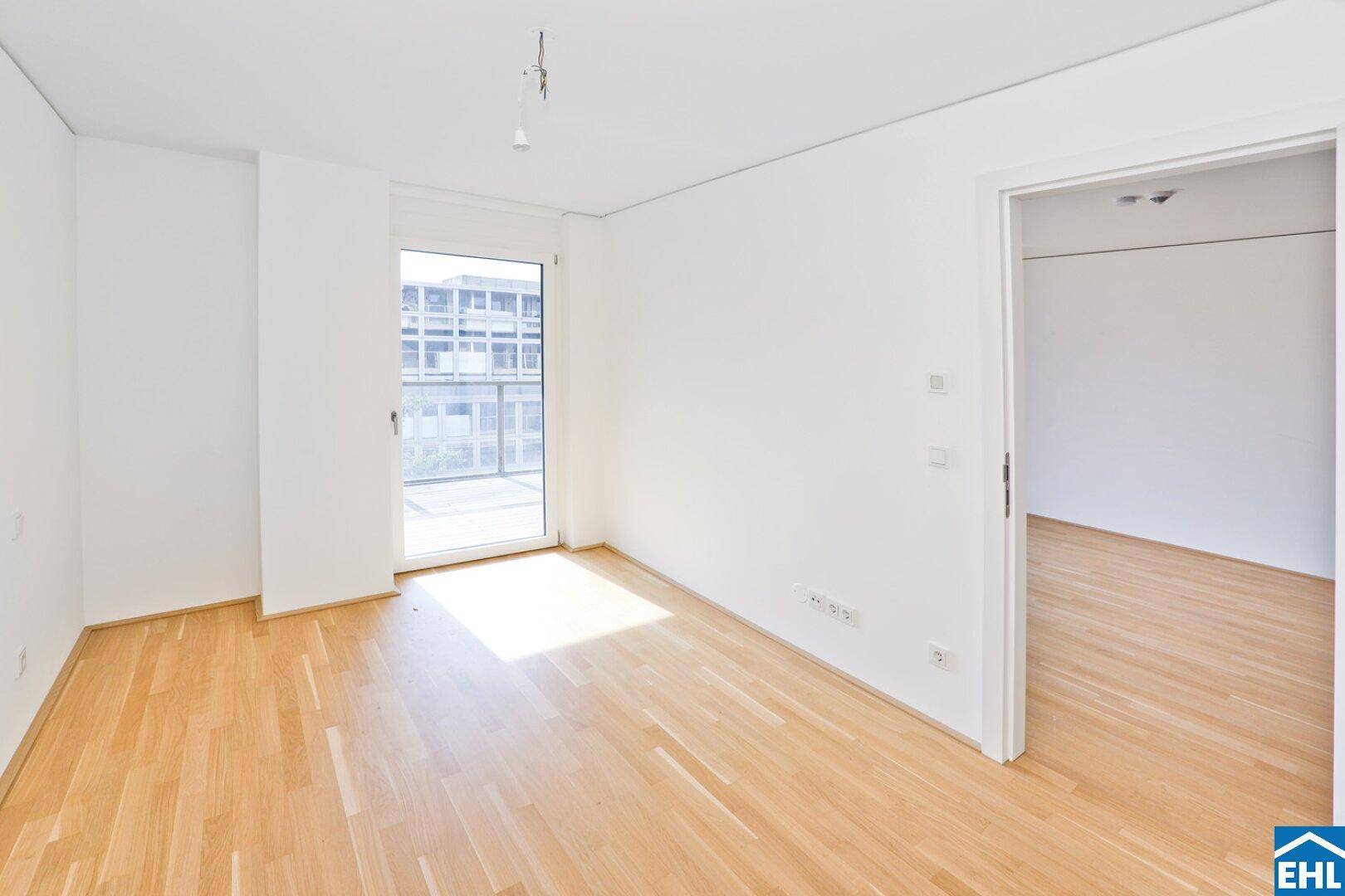 Heller, leerer Raum mit hellem Parkettboden und Zugang zu einem Balkon, ideal als Wohnbereich.