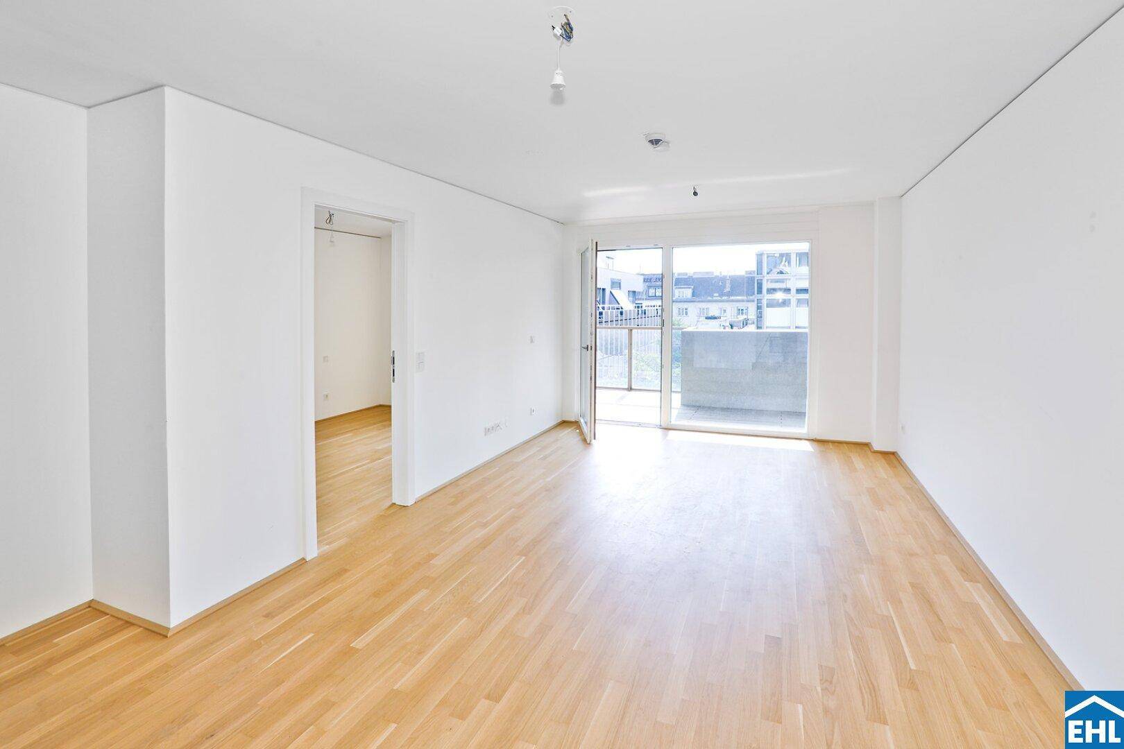 Geräumiger, heller Raum mit Parkettboden und großem Schiebetürzugang zu einem Balkon.