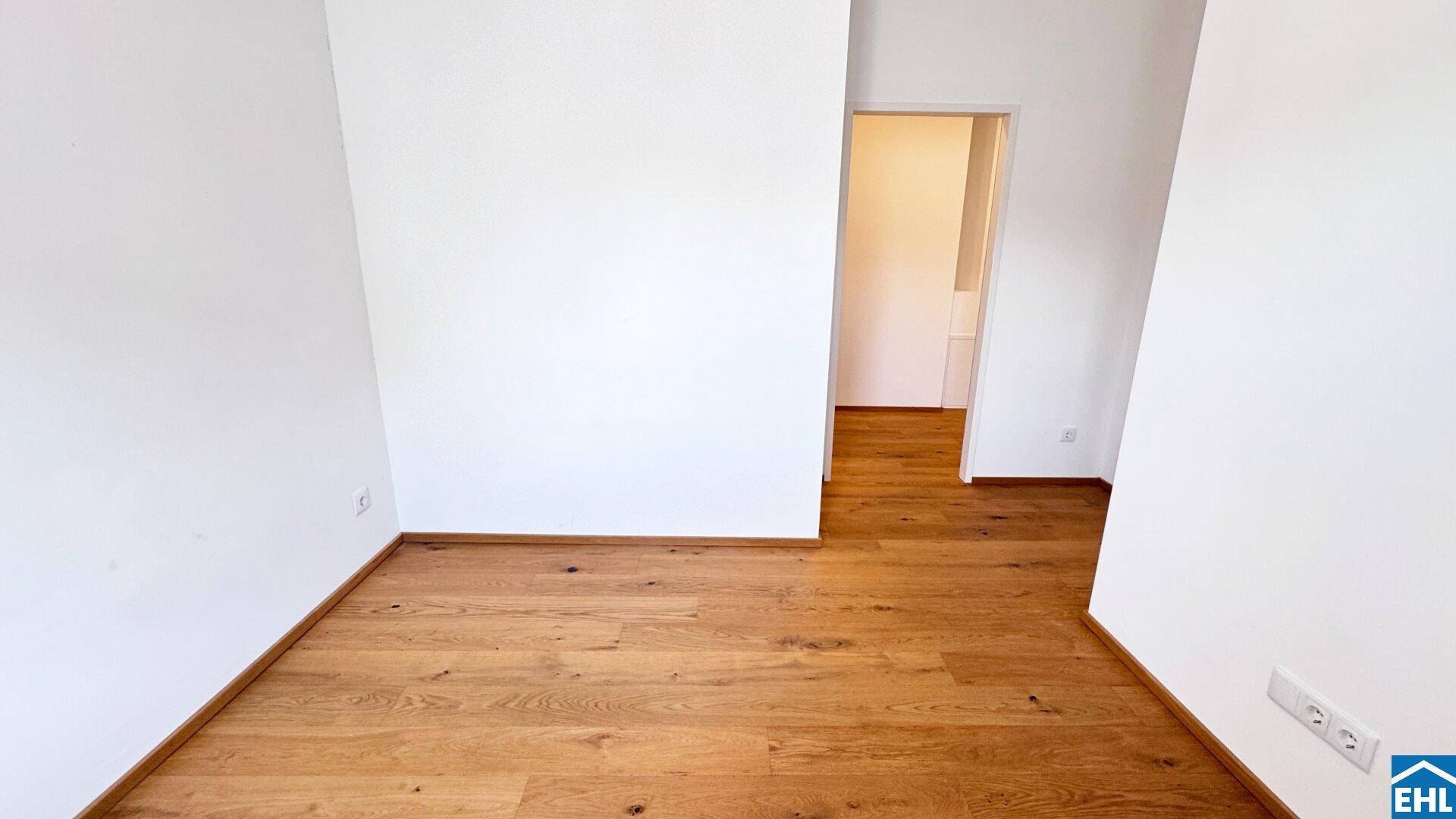 Einfaches Zimmer mit Holzboden und weiß gestrichenen Wänden.