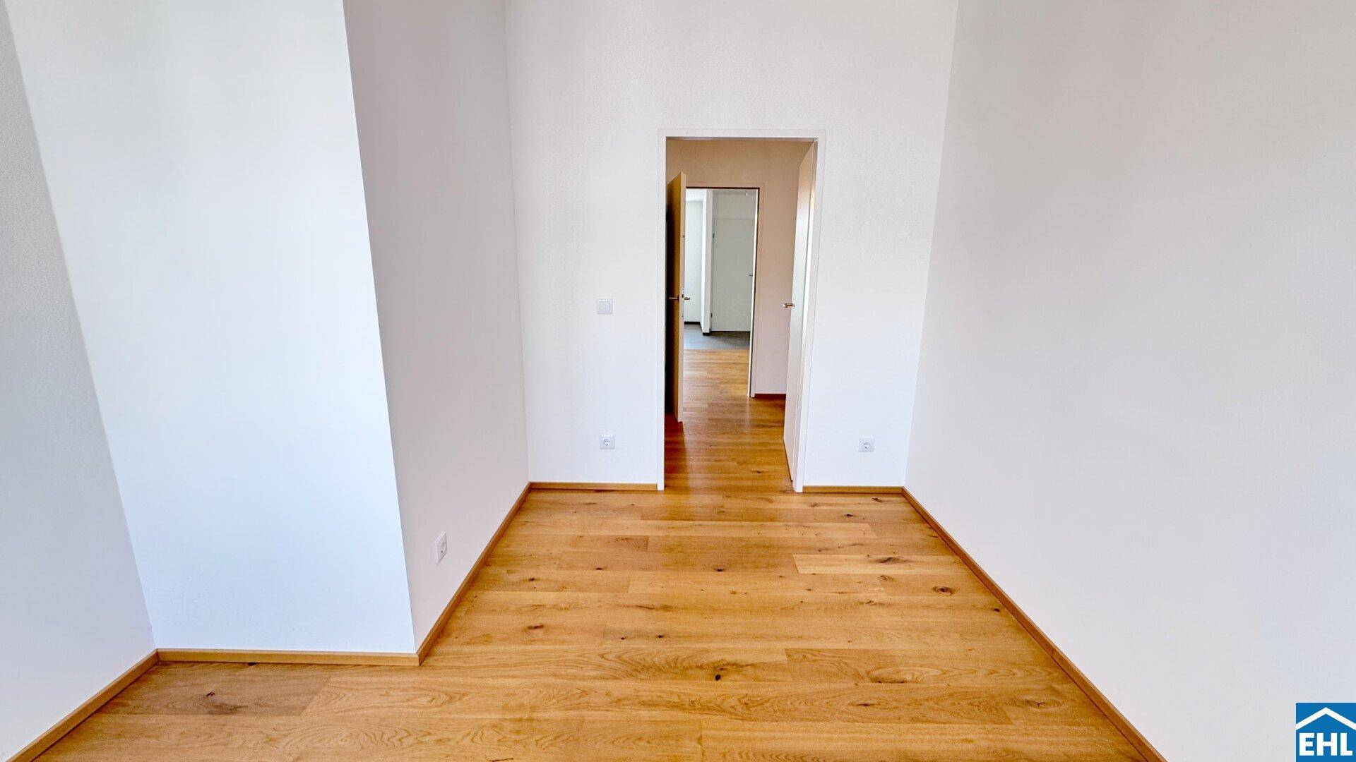 Geräumiges Zimmer mit Holzboden und Blick in den Flur.