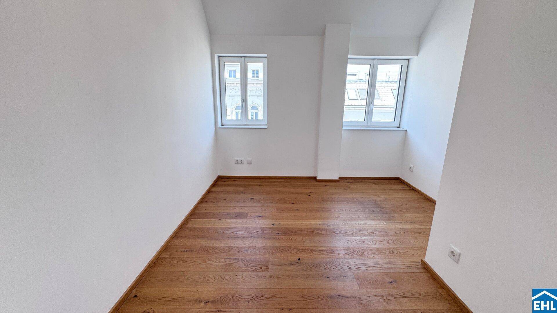 Helles Zimmer mit zwei Fenstern und Holzboden, viel Tageslicht.
