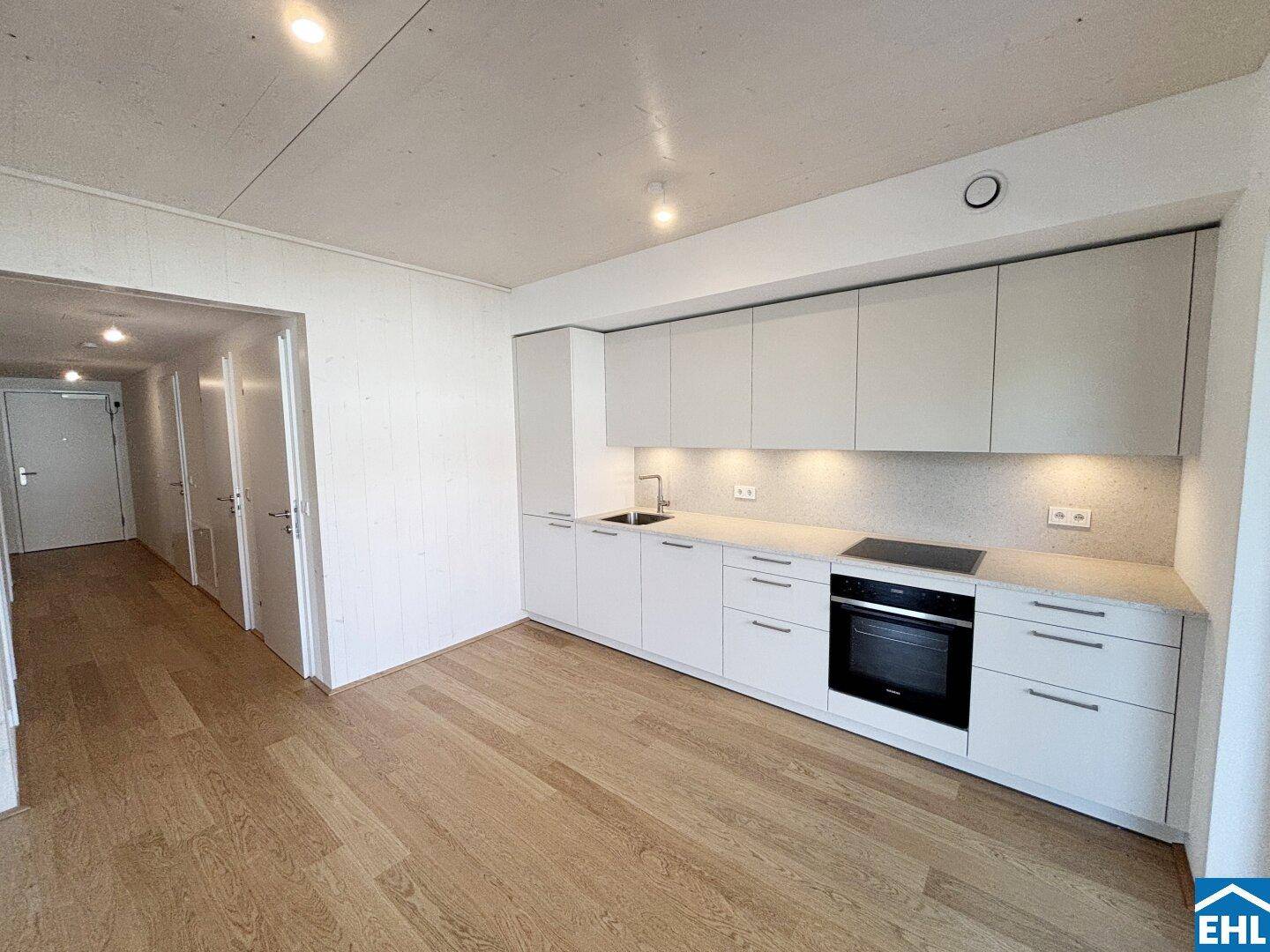Moderne Küche mit integrierten Geräten und Blick in den Flur eines Neubaus.