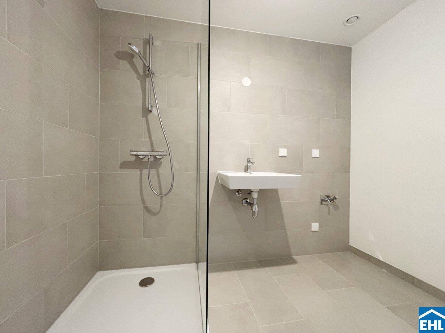 Modernes Badezimmer mit ebenerdiger Dusche, hellen Fliesen und Wandwaschbecken.