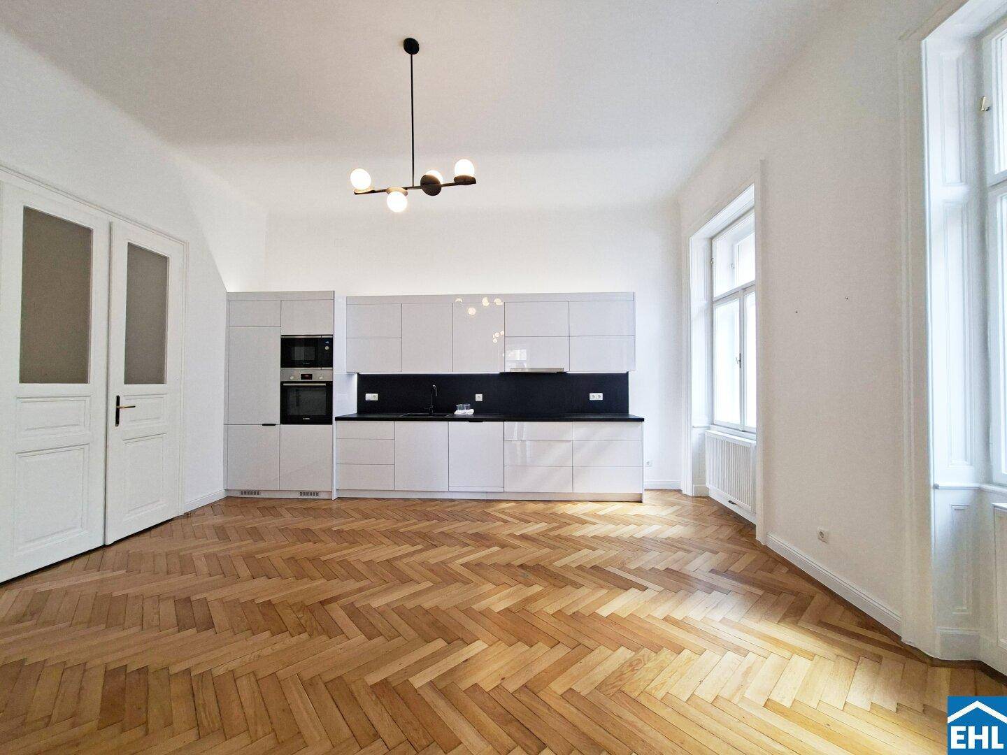 Moderne Einbauküche mit weißen Schränken, integrierten Geräten und elegantem Fischgrätparkett.