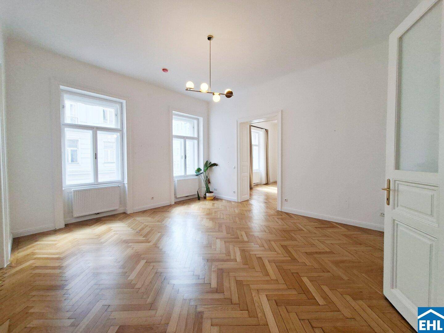 Helles Wohnzimmer mit Fischgrätparkett, hohen Decken und Blick in angrenzende Räume.