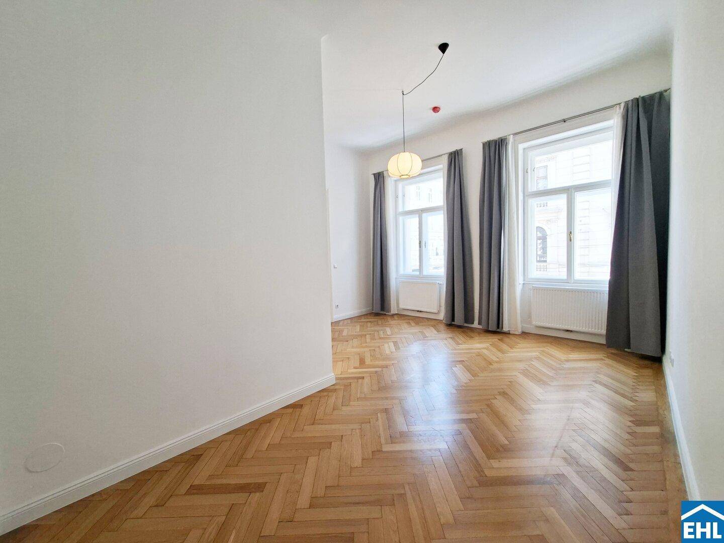 Geräumiges Schlafzimmer mit Fischgrätparkett, hohen Decken und großen Fenstern.